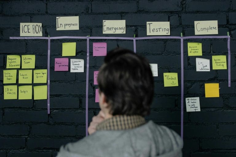 A man in an office reviews a scrum task board filled with sticky notes, planning strategy and organization.