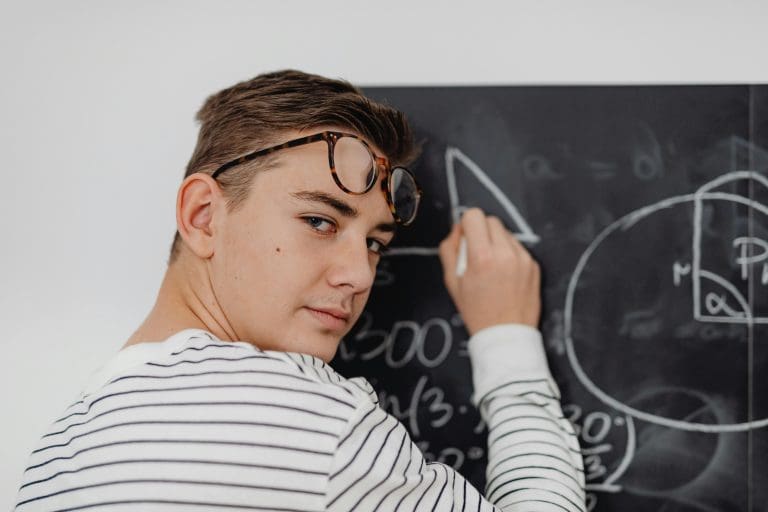 Teen boy writing math equations on a blackboard in a classroom setting.